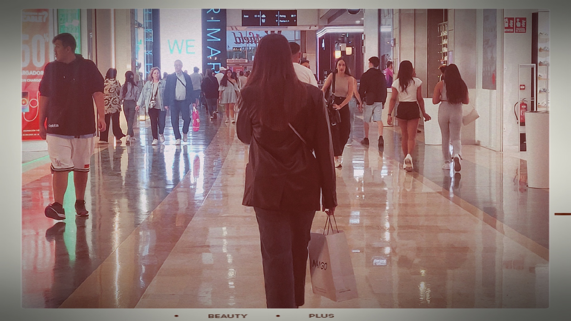 Chica de espaldas andando por un centro comercial lleno de gente diversa.